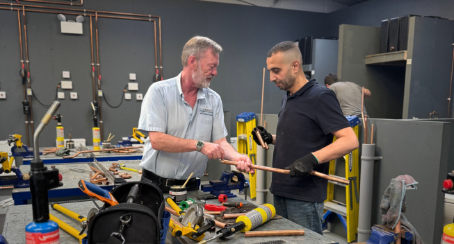 plumbing trainer showing his student a copper pipe