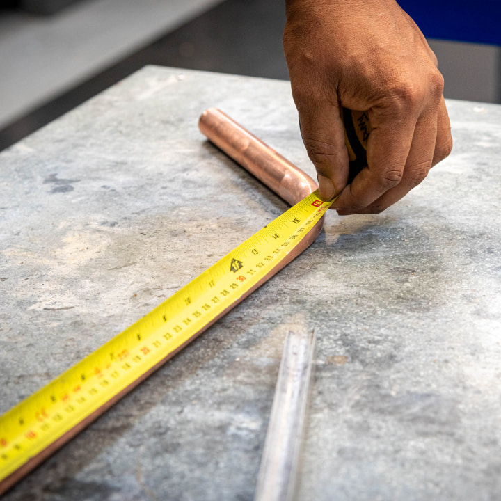 person measuring a copper pipe with a tape measure