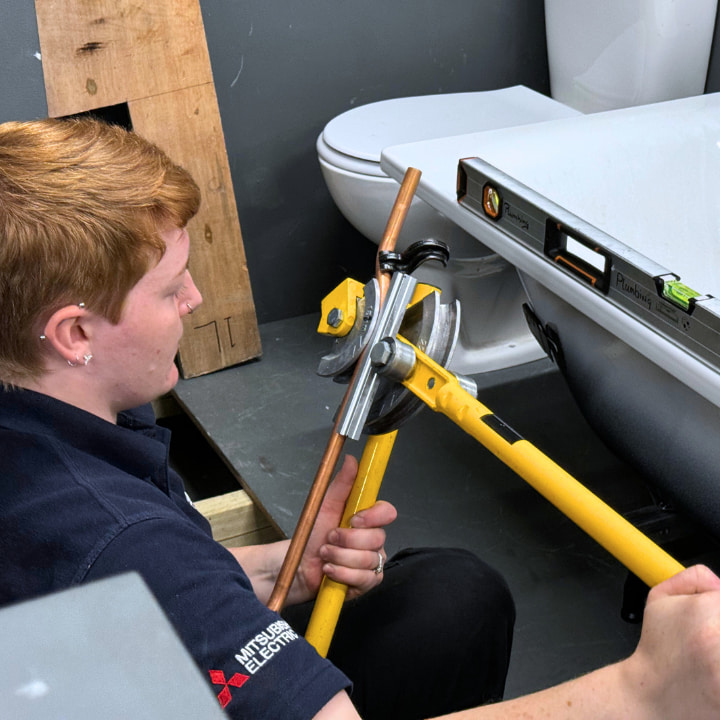 A Logic4training Plumbing NVQ student bending copper pipe in a bathroom task