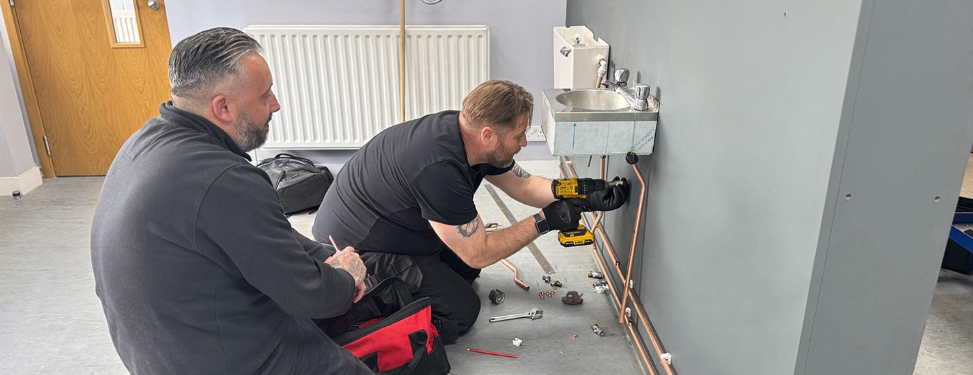 a plumbing trainer observing a plumbing student work on a sink