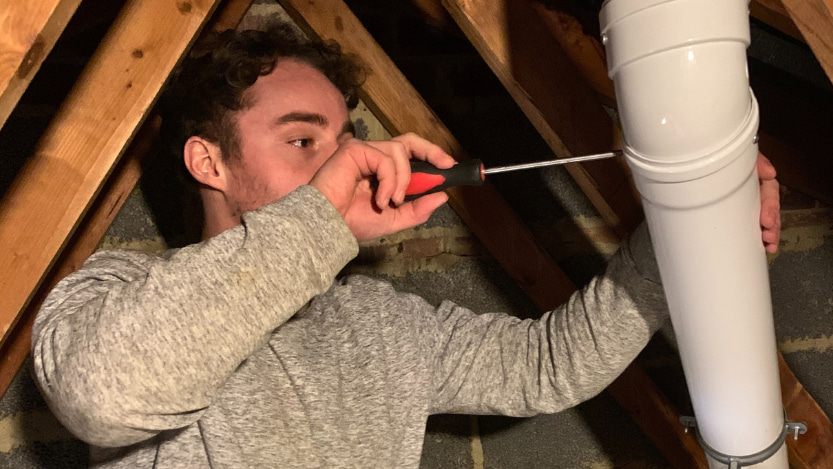 a person fixing a boiler's flue in a cramped loft