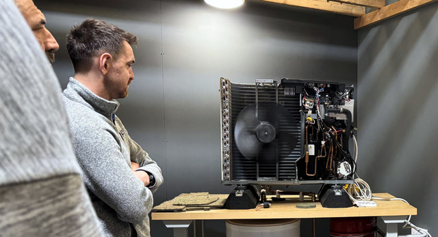 Installer observing a working air source heat pump unit during practical BUS‑ready training at Logic4training