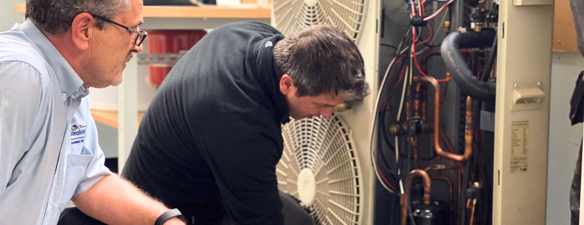 Trainer and installer working hands‑on on an air source heat pump unit during Logic4training’s practical BUS preparation course