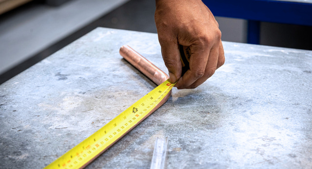 A tradesperson, with insurance, measuring copper pipe as part of their job